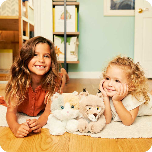 Image 100: Sisters smiling and laying down with Soft Warm Weighted Bobcat Plush Warmies